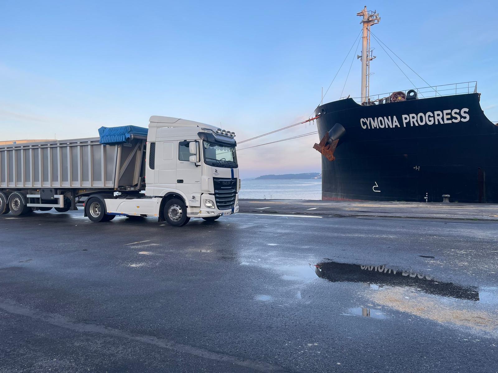Camión con bañera basculante para transporte de materia prima junto a un buque
